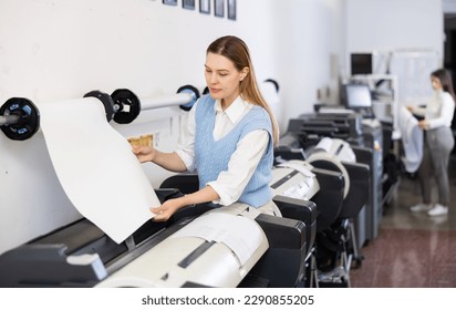 Woman working in publishing facility, loading large format paper in printer. - Shutterstock ID 2290855205