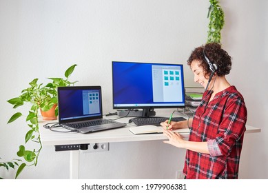 Woman working remotely standing up, wearing headset and taking notes on her pad