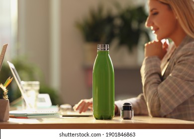 Woman working at table in modern office, focus on green thermos bottle