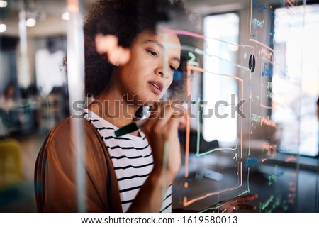 Woman working and writing on the glass board in office. Business, technology, research concept