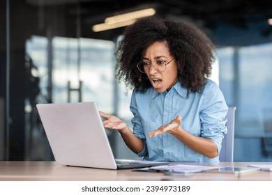 Woman at the workplace inside the office is not satisfied with the work of the computer, a frustrated businesswoman is shouting at a broken laptop, and overpriced broken software.