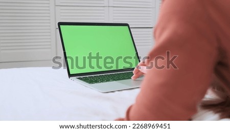 Woman works behind laptop in lying on a bed on a white sheet. Green screen, chroma key, typing on the keyboard, touchpad. Concept of remote work, study, comfortable workplace.