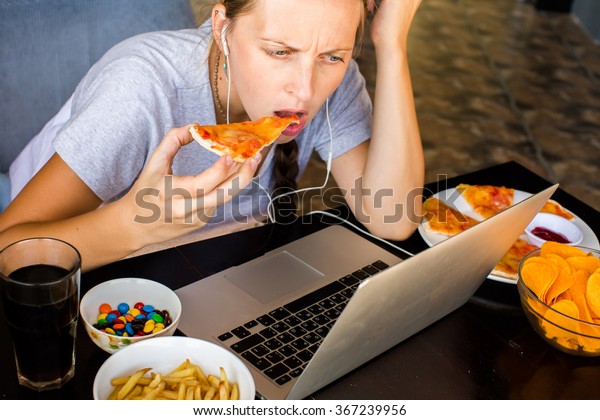 Woman works at the computer and eating fast\
food. Unhealthy Lifestyle