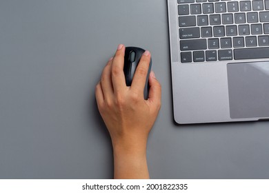 woman works with a laptop at home and holds a computer mouse in her left hand.