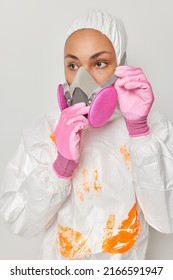 Woman Works On Chemical Plant Wears Protective Suit With Hood And Respirator Discovers Product Looks Thoughtfully Away Isolated Over Grey Background. Coronavirus And Epidemic Virus Treatment Concept