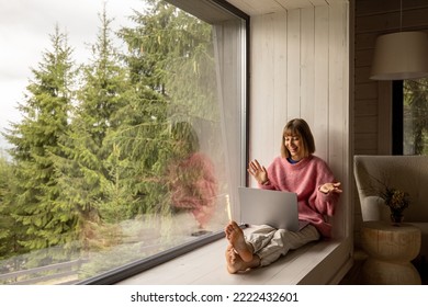 Woman works on laptop while sitting on a window with great view on mountains. Remote work from cozy place and escaping to nature concept - Powered by Shutterstock