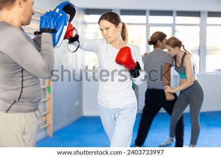 Woman works out strength and speed of boxing punch mitts with help of male partner in boxing paws. Man performs role of target and mannequins during training strike technique Stock photo © 