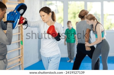 Woman works out strength and speed of boxing punch mitts with help of male partner in boxing paws. Man performs role of target and mannequins during training strike technique Stock photo © 