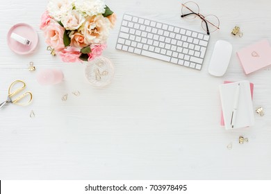 Woman workspace with computer, pink and beige roses flowers bouquet, accessories, diary, glasses on white background. Lay Flat home office desk. Top view feminine background.