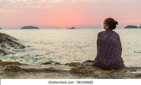 Woman wrapped in plaid sits lonely on the coast.