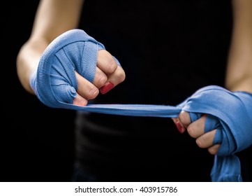 Woman is wrapping hands with blue boxing wraps. Self Defense for Women. Isolated on black with red nails. Strong hand and fist, ready for fight and active exercise - Powered by Shutterstock