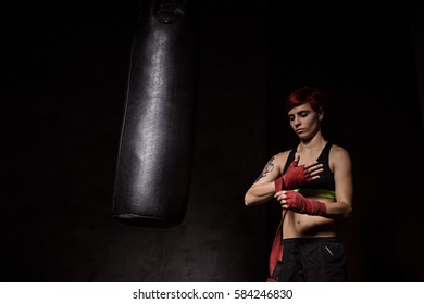 Woman is wrapping hands with red boxing wraps in dark room - Powered by Shutterstock