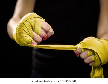 Woman Is Wrapping Hands With Yellow Boxing Wraps. Self Defense For Women. Isolated On Black With Red Nails. Strong Hand And Fist, Ready For Fight And Active Exercise