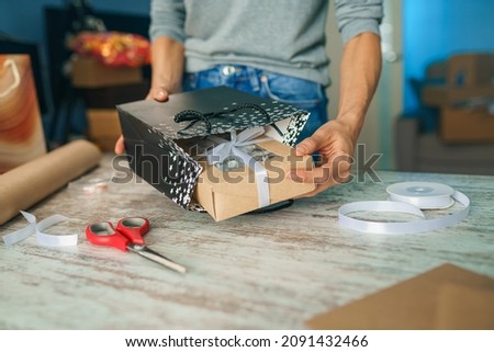 Woman wrapping holyday gift, decorating stylish gift in craft paper on table in home
