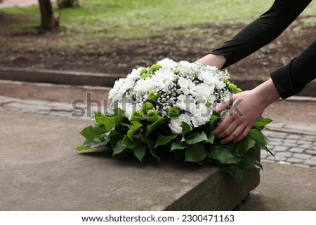 Woman with wreath of flowers near tombstone outdoors, closeup. Funeral attribute