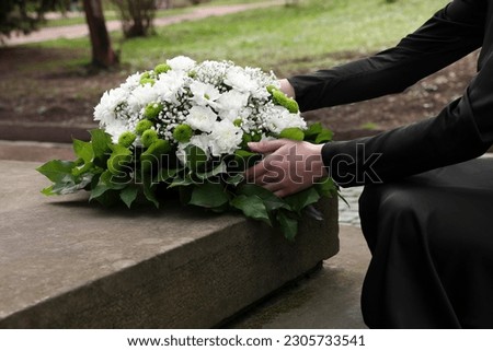 Woman with wreath of flowers near tombstone outdoors, closeup. Funeral attribute