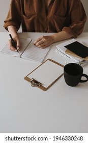 Woman write in a blank sheet notebook. Minimalist home office desk workspace with coffee cup, clipboard. Work, business background.