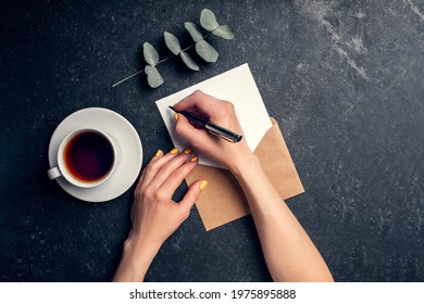 Woman writes letter on black background top view