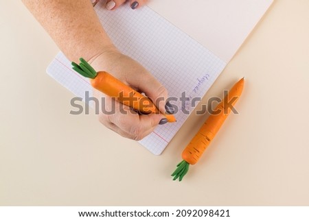 Woman writes with pen in handmade carrot shaped casing at beige table upper view