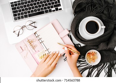 Woman Writes In The Planner. Workspace With Laptop,  Coffee Cup Wrapped In Scarf, Golden Clips, Glasses. Stylish Office Desk. Autumn Or Winter Concept.  Flat Lay, Top View 