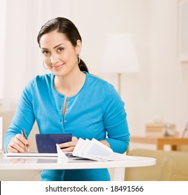 Frau schreibt Scheck aus dem Scheckbuch, um monatliche Rechnungen zu bezahlen
