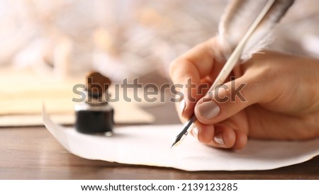 Woman writing in ink on paper sheet at table, closeup