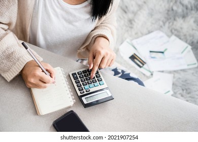 woman writing a list of debt on notebook calculating her expenses with calculator with many invoices , female hand doing accounting  - Shutterstock ID 2021907254