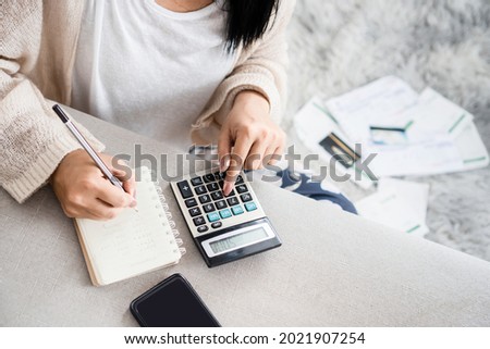 woman writing a list of debt on notebook calculating her expenses with calculator with many invoices , female hand doing accounting 