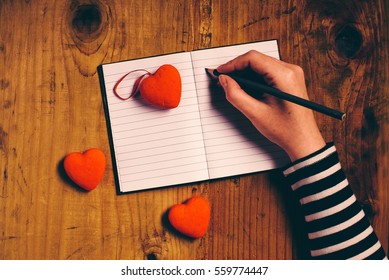 Woman writing love letter card for Valentines day, top view of female hands, retro toned