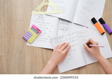 Woman writing math formulas in copybook on wooden table