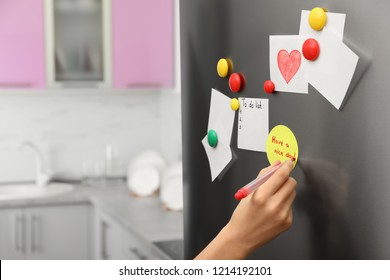 Woman Writing Message On Note Stuck To Refrigerator Door At Home, Closeup