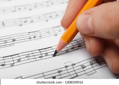 Woman Writing Music Notes On Sheet With Pencil, Closeup