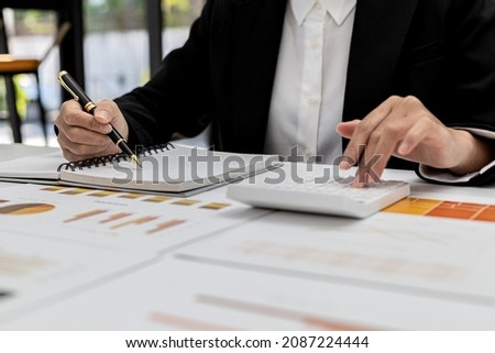 A woman is writing a note on a notebook and pressing a white calculator to calculate the amount to be recorded, the finance worker is preparing the paperwork. Concept of company financial management.