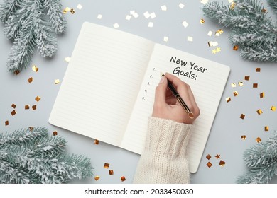 Woman writing in notebook at light grey table with Christmas decor, top view. New Year aims