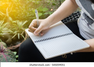 Woman Writing A Notebook With Outside In Evening Time.