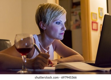 woman writing notes from laptop while she is drinking wine - Shutterstock ID 697945366
