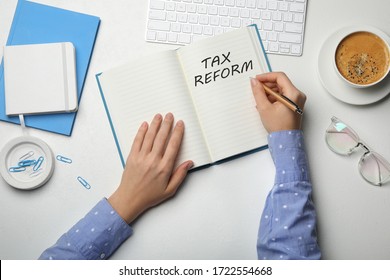 Woman Writing Phrase TAX REFORM In Notebook At White Table, Top View