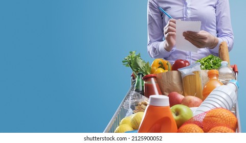 Woman Writing A Shopping List And Trolley Full Of Fresh Goods, Grocery Shopping Concept