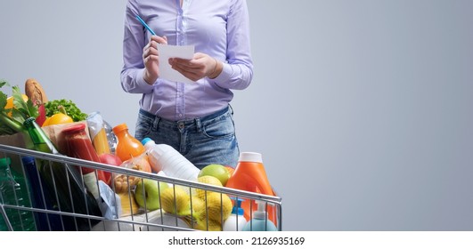 Woman Writing A Shopping List And Trolley Full Of Fresh Goods, Grocery Shopping Concept