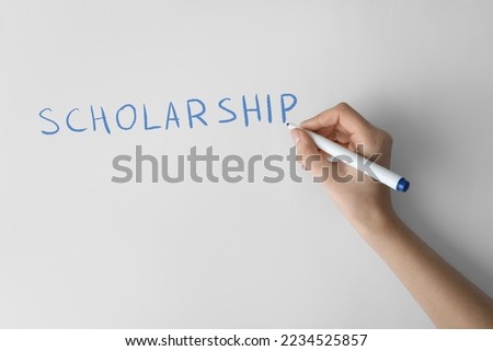 Woman writing word SCHOLARSHIP on white paper, closeup