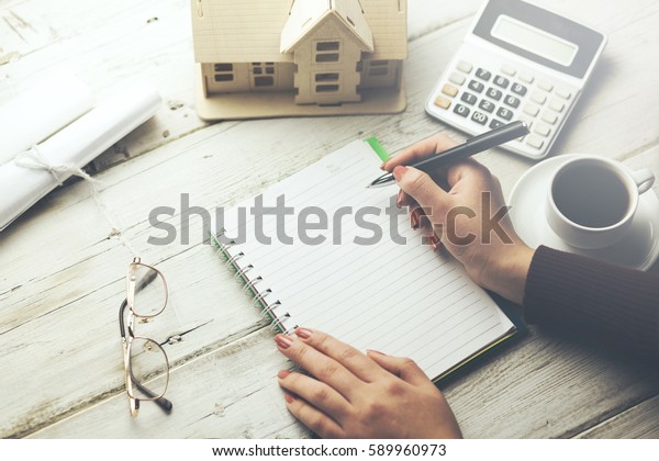 woman written notepad with house model and\
calculator on table