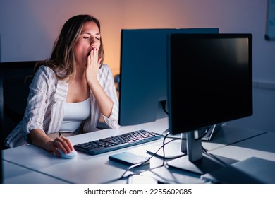 Woman yawning while sitting at her office desk, tired while working overtime late at night - Shutterstock ID 2255602085