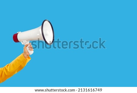 Woman yelling through megaphone. Young lady with amplified voice sharing important information. Human hand holding white loudspeaker on blue colour studio background with empty copyspace on right side