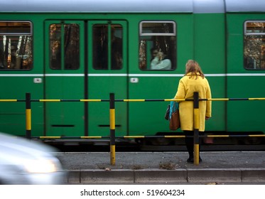 Woman in yellow coat and a green tram and a car passing in motion blur