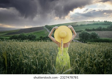 A woman in a yellow dress in a field of wheat admiring the clouds and the sunset - Shutterstock ID 2327478781