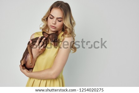 A woman in a yellow dress holds a dog in her hand              