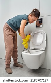 A woman in yellow gloves cleans the toilet bowl with a brush and detergent, the concept of house cleaning and household chores - Shutterstock ID 2198907127