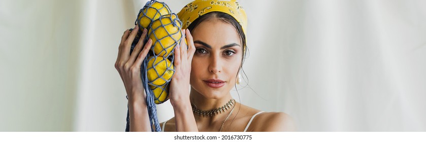 woman in yellow headscarf holding string bag with lemons on white, banner