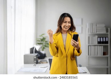 A woman in a yellow jacket is holding a cell phone and smiling. She is in a professional setting, possibly at work - Powered by Shutterstock