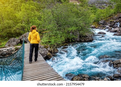 Woman in yellow jacket standing on a suspension bridge over mountain river in Norway